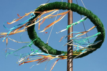 Ein Maibaumkranz mit bunten Bändern an einem Holzmast gegen einen klaren blauen Himmel, traditionelles Symbol des Frühlings und der Maifeier in Deutschland.